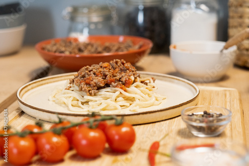 Plate with boiled spaghetti served with fried minced meat standing on wooden table with fresh tomatoes and pepper