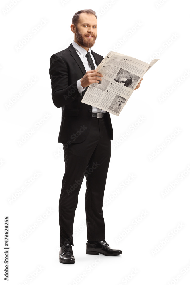 Full length shot of a young professional man in a suit standing with a newspaper and smiling at camera Full length shot of a young professional man in a suit standing with a newspaper and smiling at camera