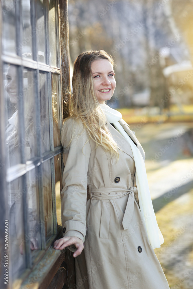 Fototapeta premium young blond slavic woman with long hair wearing trench coat close up street portrait on city park background
