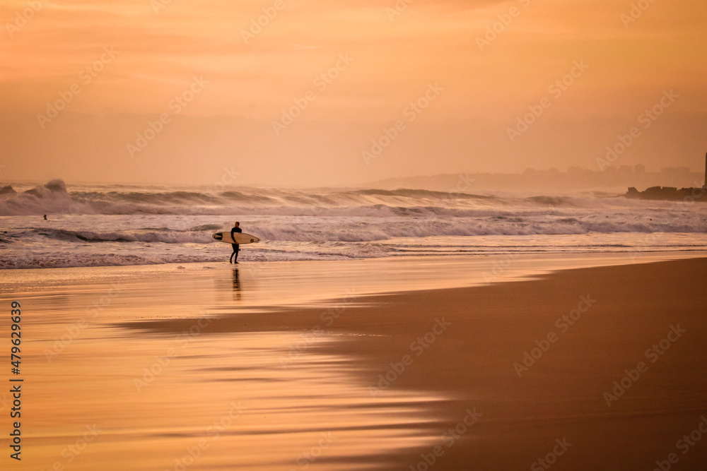 surfer returns from water with a surfboard at the sunset