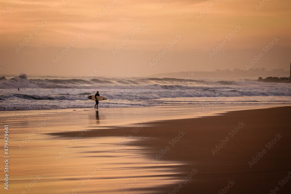 Fototapeta premium surfer returns from water with a surfboard at the sunset