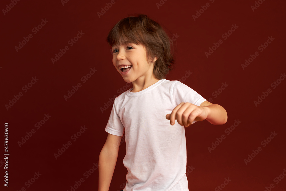Side view studio shot of handsome active full of energy cheerful restless boy of 6, moving around, dancing, jumping or running, laughing, feeling good, isolated on red. Carefree kids Side view studio shot of handsome active full of energy cheerful restless boy of 6, moving around, dancing, jumping or running, laughing, feeling good, isolated on red. Carefree kids