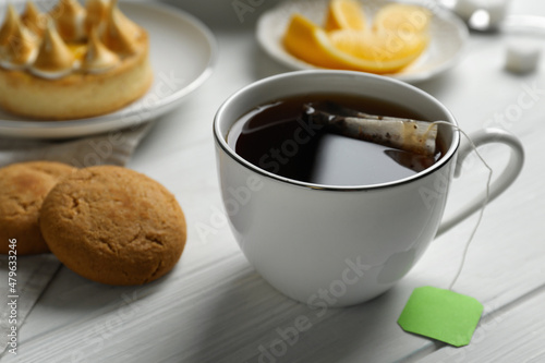 Tea bag in cup of hot water and cookies on white wooden table