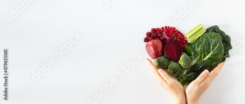 Colorful heart shape from various fruits and vegetables with human hands holding it isolated on white background. Healthy plant-based food concept. Copy space for text. Top view. Love for fresh food.