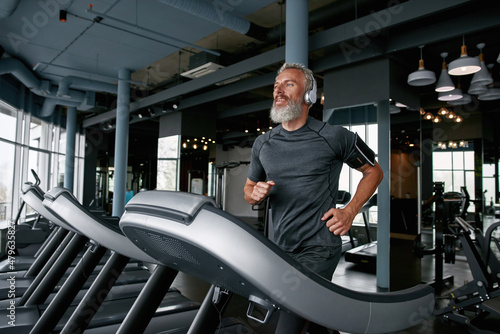 Schilderij op canvas Active senior man jogging on treadmill in sports center