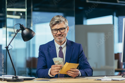 Fototapeta Senior experienced banker looks at the camera and smiles, businessman holds an e