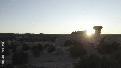 Drone push in reveals the sun behind a small desert rock formation