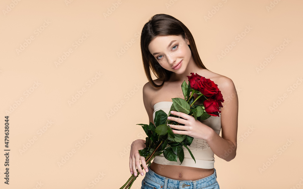 pleased young woman in crop top holding red roses isolated on beige pleased young woman in crop top holding red roses isolated on beige
