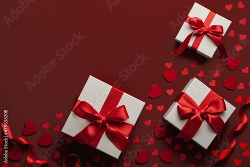 Presents with red bow on red background with heart confetti. Flat lay style. Valentine day concept. Saint VAaentines