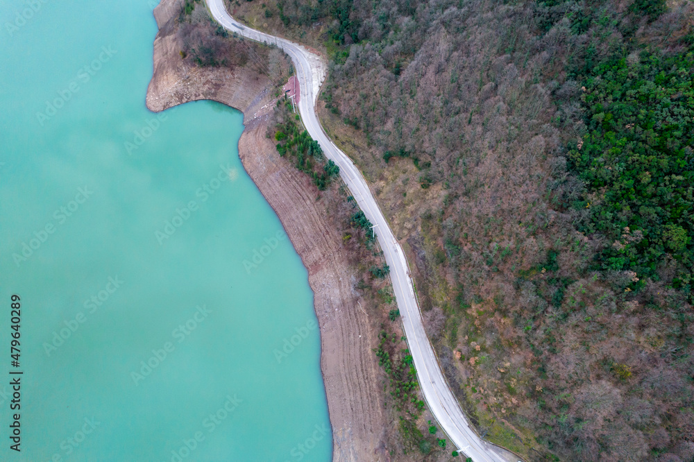 Long road between lake and forest. Aerial top view.