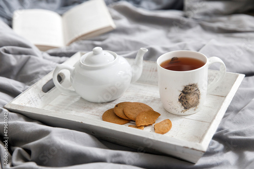 interior and home cosiness concept. Top view. A cup of tea  a teapot with herbal tea  sugar bowl on a wooden tray on the bed