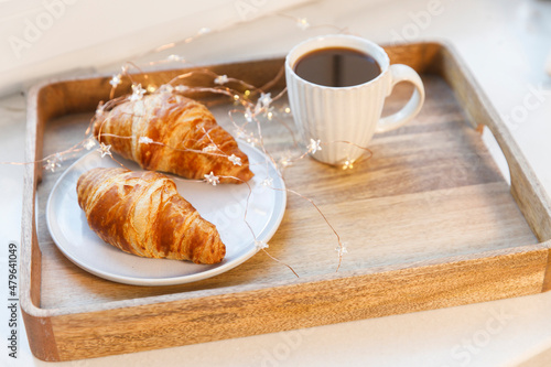 Fototapeta Naklejka Na Ścianę i Meble -  Freshly baked croissant on a gray round plate, white cup with coffee and garland on a tray on the table