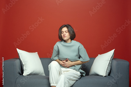 Unhealthy woman touch stomach suffer abdominal pain indigestion or menstrual period ach, sitting on sofa