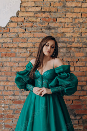 A beautiful girl in a green dress smile shows a brick wall dress