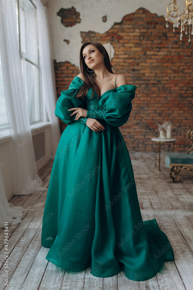 Fototapeta premium A beautiful girl in a green dress smile shows a brick wall dress