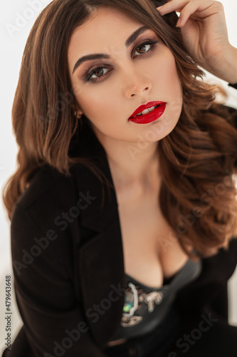 Fashion portrait of a sexy beautiful young woman with professional makeup  red lips and brunet hair in stylish black clothes with breasts on a white background
