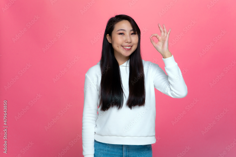 Asian confident young girl showing hand gesture ok sign recommend product or service on pink studio background Asian confident young girl showing hand gesture ok sign recommend product or service on pink studio background