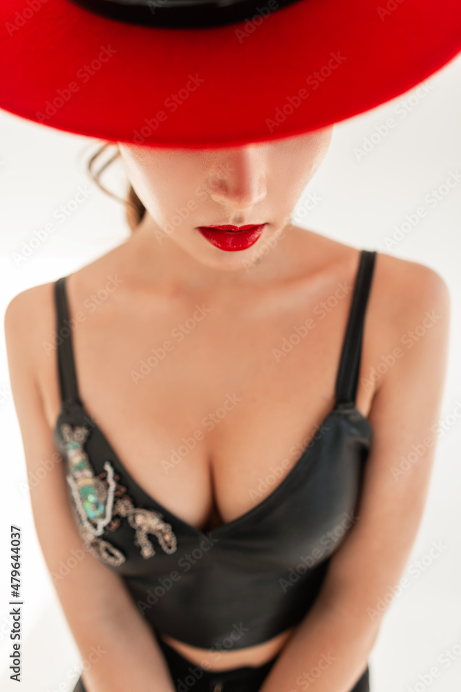 Pretty glamorous young sexy girl with red lips and a hat in black fashionable clothes look and top with beautiful breasts on a white background in studio Pretty glamorous young sexy girl with red lips and a hat in black fashionable clothes look and top with beautiful breasts on a white background in studio
