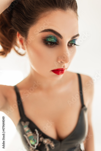 Lovely young sexy woman model with colorful professional makeup, red lips and green eyelids in fashionable clothes with beautiful breasts on a white background in the studio