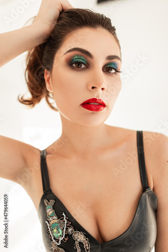 Beautiful sexy woman with bright makeup and red lips with curly hair in fashionable clothes with a leather black top on a white background in the studio