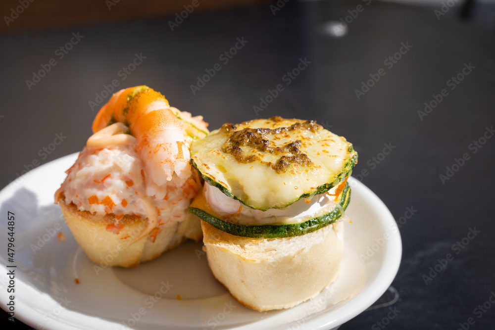 Delicious Spanish tapas on plate with bread, prawn, cheese and zucchini on top. Restaurant food, bar snack, gourmet concepts Delicious Spanish tapas on plate with bread, prawn, cheese and zucchini on top. Restaurant food, bar snack, gourmet concepts