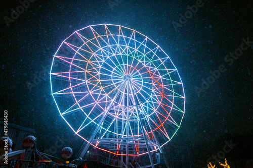 Cool neon ferris wheel illuminated in the park in snowy weather at night. Amazing park