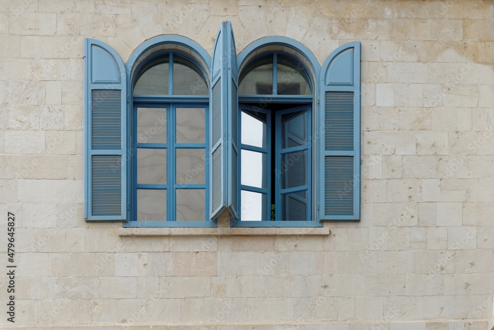 Open windows of the stone building with blue frame and blue wooden blinds