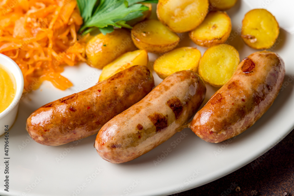 Fried hunter sausage with potatoes, fried cabbage and mustard on white plate on dark brown table macro close up Fried hunter sausage with potatoes, fried cabbage and mustard on white plate on dark brown table macro close up