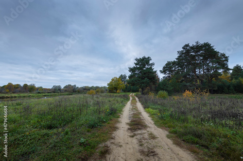 Dirt road along the river bank. Cloudy autumn weather. Rural landscape with road  river and autumn forest.