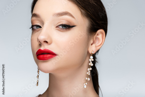 confident woman in earrings with bright makeup looking at camera isolated on grey