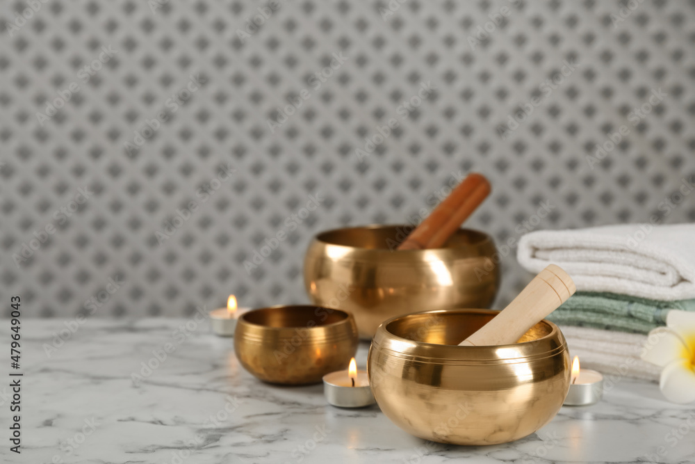 Tibetan singing bowls, mallets, towels and burning candles on white marble table, space for text