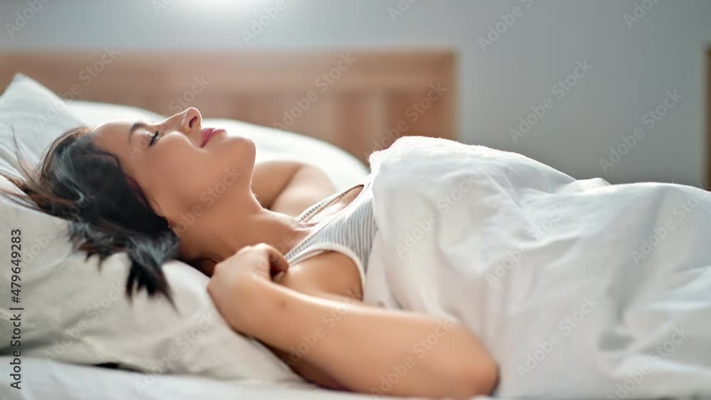 Lazy morning woman smiling stretching body awake in comfortable bed surrounded by natural sum light Lazy morning woman smiling stretching body awake in comfortable bed surrounded by natural sum light