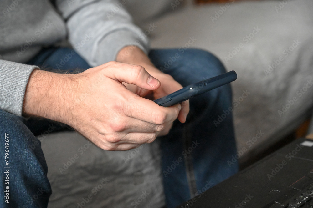 Man with modern mobile phone in hands. Man's hands holding smartphone. Young man touching screen of mobitel in his office. Man using smart phone at home.