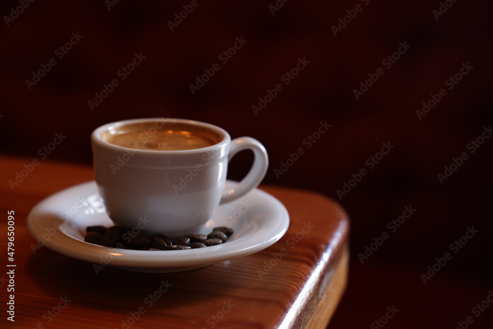 Cup of hot aromatic coffee and roasted beans on wooden table in cafe. Space for text Cup of hot aromatic coffee and roasted beans on wooden table in cafe. Space for text