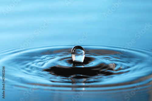 Large oval splash of blue water drop. There are air bubbles in the drop. Vibrations as circles on the surface