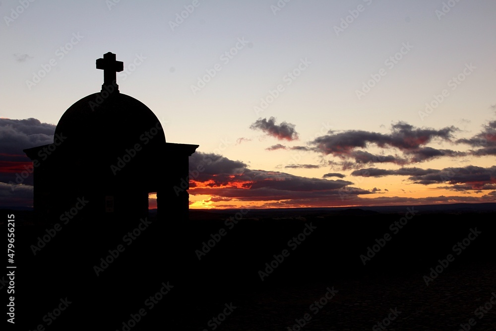 small building with a christian cross on top with a sunset in the background in red and orange tones attempts