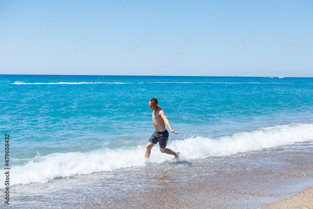 Attractive young man with a beautiful body in shorts walks along the sandy seashore and enjoying summer vacation Attractive young man with a beautiful body in shorts walks along the sandy seashore and enjoying summer vacation