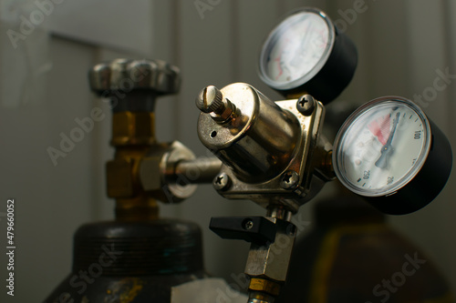 view of switch devices, indicators and a gas pressure regulator, liquids mounted on a metal gas cylinder at the window in a dark room of an industrial premises