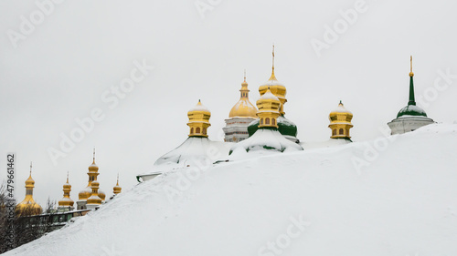 Photography Golden domes of Kiev Pechersk Lavra or Kyiv Monastery of Caves behind a snowy slope on cold winter day