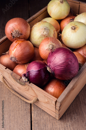 Onions in old box on rustic wooden table, food ingredients