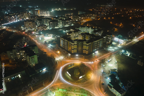 Aerial view of high rise apartment buildings and bright illuminated roundabout intersection on urban street in city residential area at night. Dark urban landscape