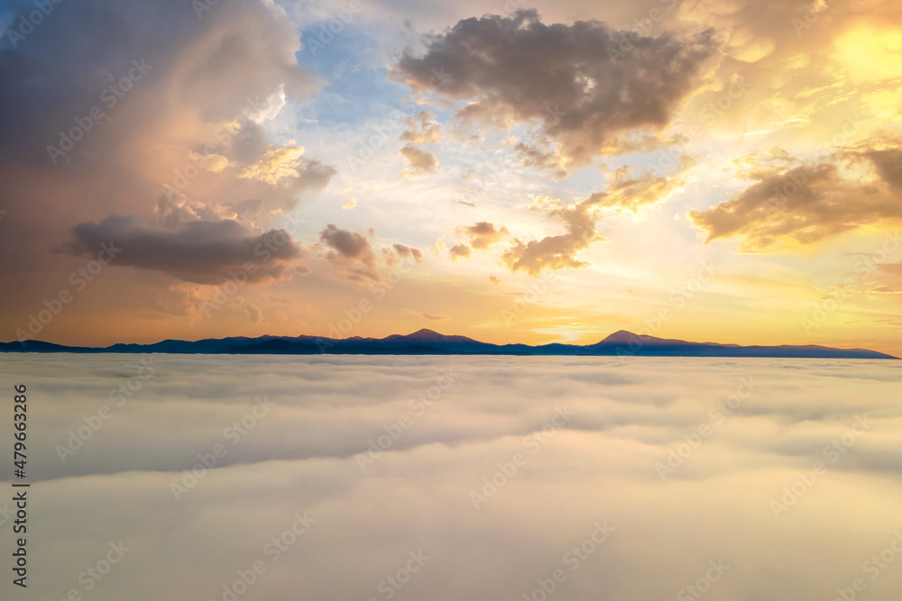 Aerial view of yellow sunset over white puffy clouds with distant mountains on horizon