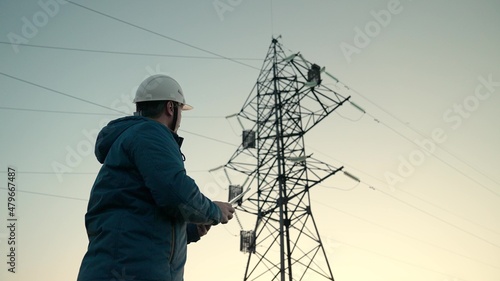 Construction of high-voltage power lines. Engineer man, power engineer in a protective helmet works on the power line using a computer tablet. Green energy concept. Electricity supply.