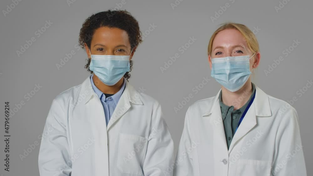 Studio Portrait Of Two Female Doctors Or Lab Workers Wearing Face Masks In White Coats Studio Portrait Of Two Female Doctors Or Lab Workers Wearing Face Masks In White Coats