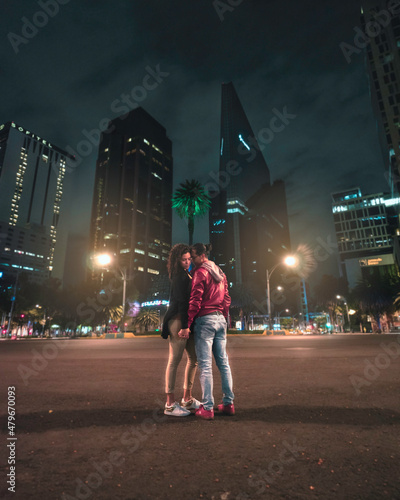 Pareja de jóvenes enamorados tomados de las manos frente a las luces nocturnas de la ciudad photo