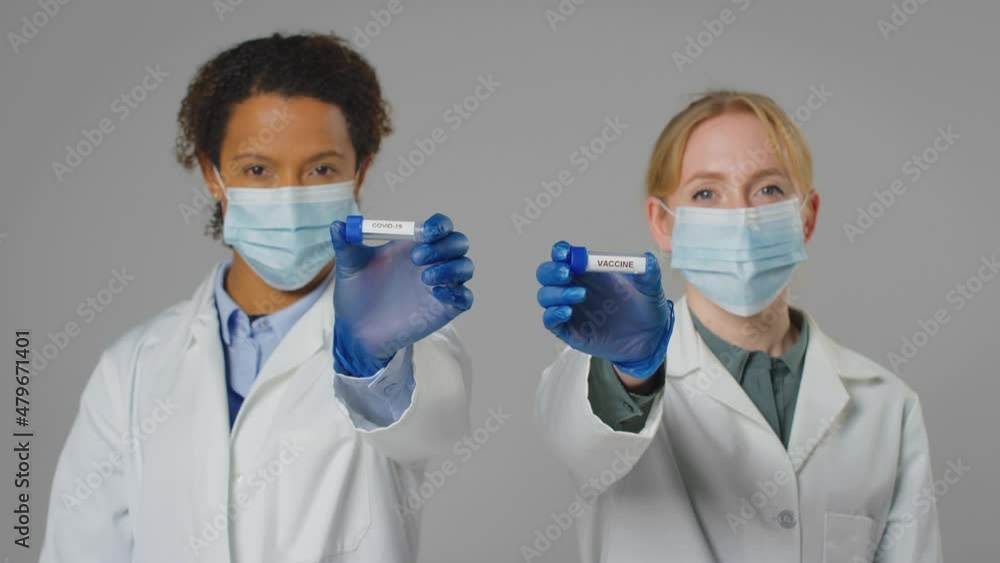 Studio Shot Of Lab Research Workers In Face Masks Holding Test Tubes Labelled Vaccine And Covid-19 Studio Shot Of Lab Research Workers In Face Masks Holding Test Tubes Labelled Vaccine And Covid-19