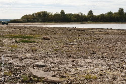 Drying bottom of the river against the background of a natural landscape - shore, trees, sky. Low water level in the reservoir.