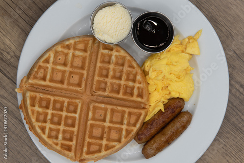 Overhead view of round waffle for tradional breakfast with sausage, eggs, syrup, and butter to fill the appetite photo