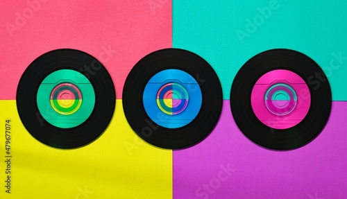 Three colorful vinyl CD discs in flat lay format displayed on a multi colored vibrant retro background.
