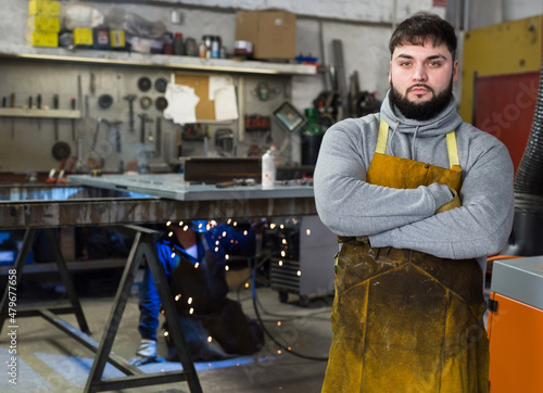 Young confident professional blacksmith standing in metalworking workshop.. photo